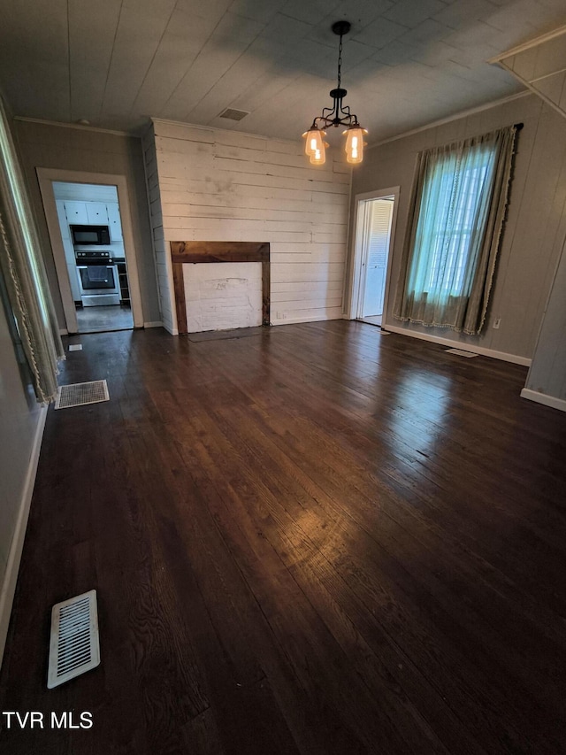 unfurnished living room featuring dark hardwood / wood-style flooring, a notable chandelier, and wood walls