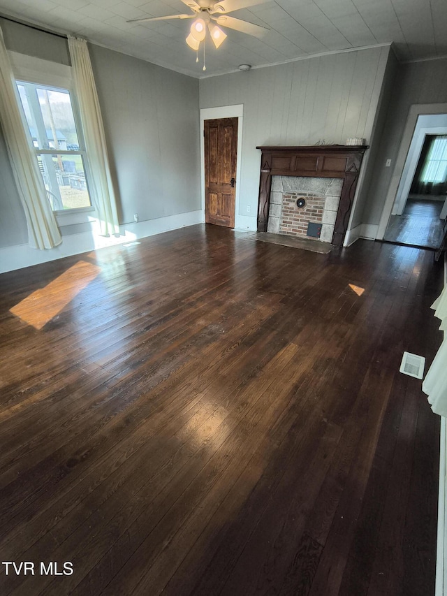 unfurnished living room featuring a stone fireplace, ceiling fan, and dark wood-type flooring