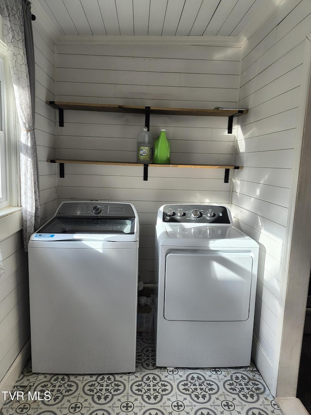 clothes washing area with washer and dryer, light tile patterned floors, and wood walls