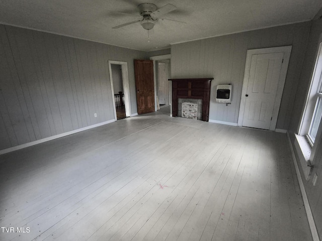 unfurnished living room featuring heating unit, ceiling fan, wood walls, and hardwood / wood-style flooring