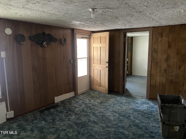 foyer featuring wood walls, dark carpet, and a textured ceiling