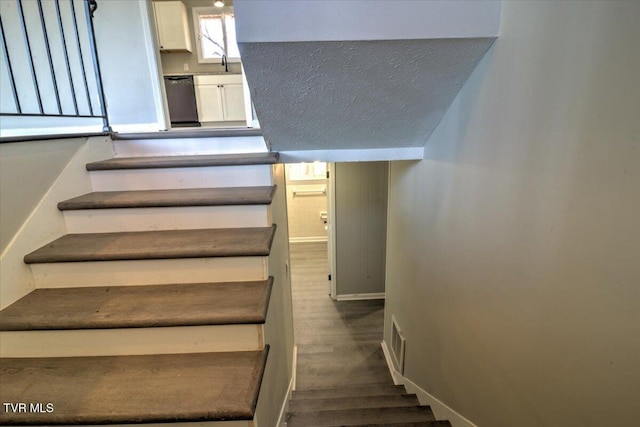 staircase featuring sink, a textured ceiling, and hardwood / wood-style flooring