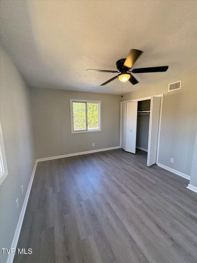 unfurnished bedroom with ceiling fan, dark hardwood / wood-style flooring, a textured ceiling, and a closet