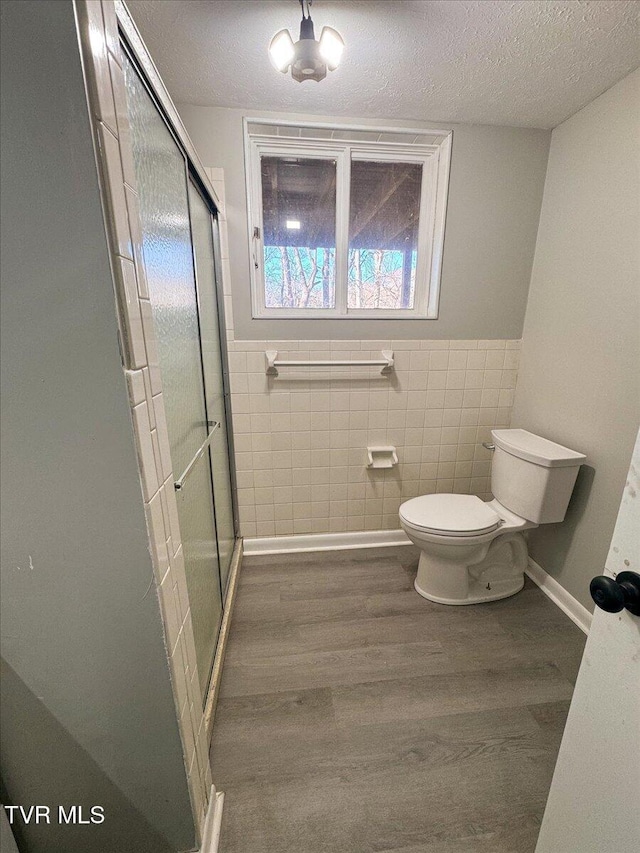 bathroom featuring a shower with door, wood-type flooring, tile walls, and toilet