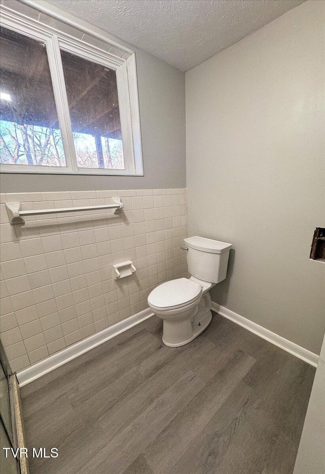 bathroom with hardwood / wood-style floors, toilet, tile walls, and a textured ceiling