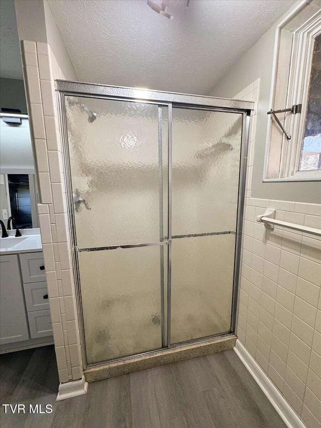 bathroom featuring hardwood / wood-style floors, a shower with door, tile walls, and a textured ceiling