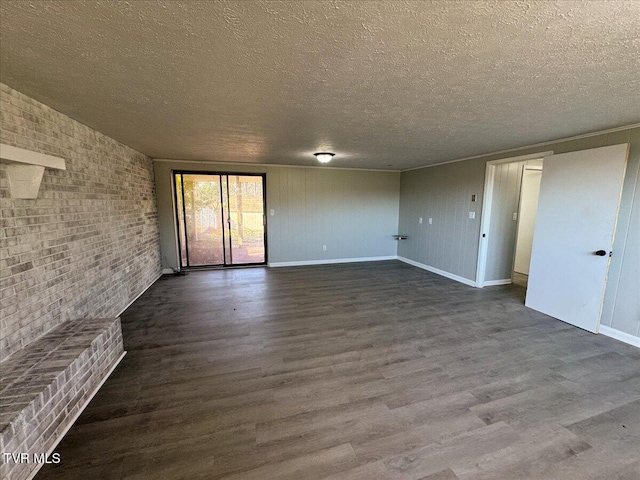 empty room featuring dark wood-type flooring, brick wall, and a textured ceiling