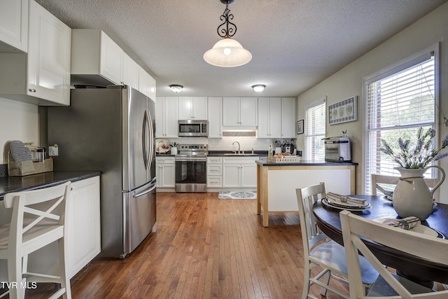 kitchen featuring pendant lighting, a textured ceiling, dark hardwood / wood-style flooring, white cabinetry, and stainless steel appliances