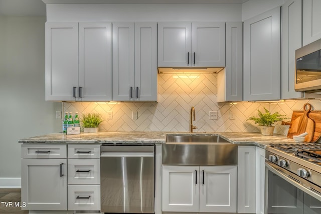 kitchen with appliances with stainless steel finishes, backsplash, light stone counters, and sink