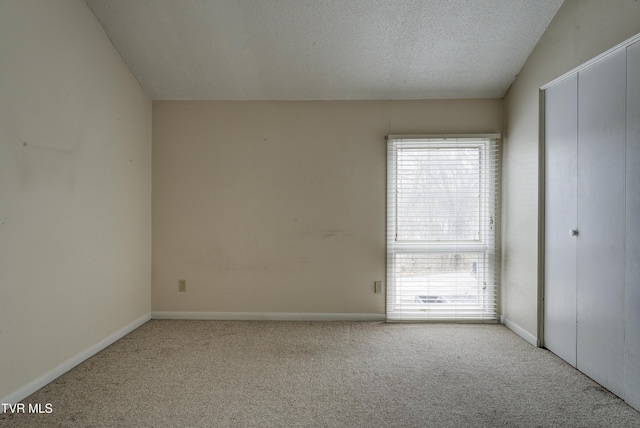 unfurnished room with a textured ceiling, light colored carpet, and vaulted ceiling