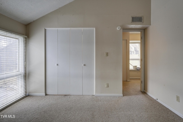 unfurnished bedroom featuring light carpet, a textured ceiling, multiple windows, and lofted ceiling