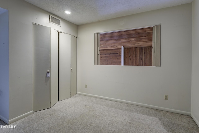 unfurnished bedroom featuring a textured ceiling, light colored carpet, and a closet