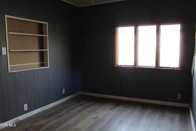 unfurnished room featuring built in shelves, plenty of natural light, wooden walls, and wood-type flooring