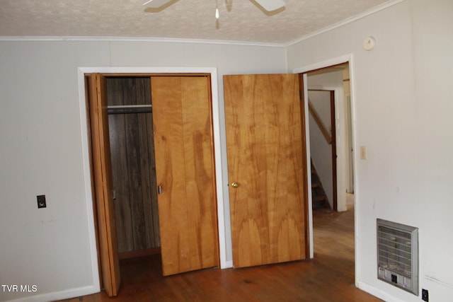 unfurnished bedroom featuring ornamental molding, a textured ceiling, heating unit, ceiling fan, and dark wood-type flooring