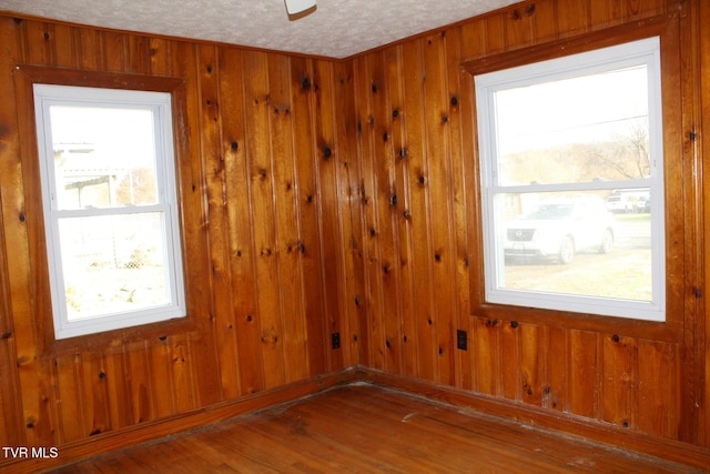 unfurnished room with hardwood / wood-style floors, a textured ceiling, ceiling fan, and wooden walls