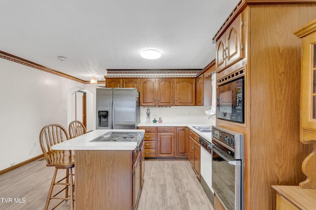 kitchen featuring stainless steel refrigerator with ice dispenser, black microwave, a center island, light hardwood / wood-style floors, and oven