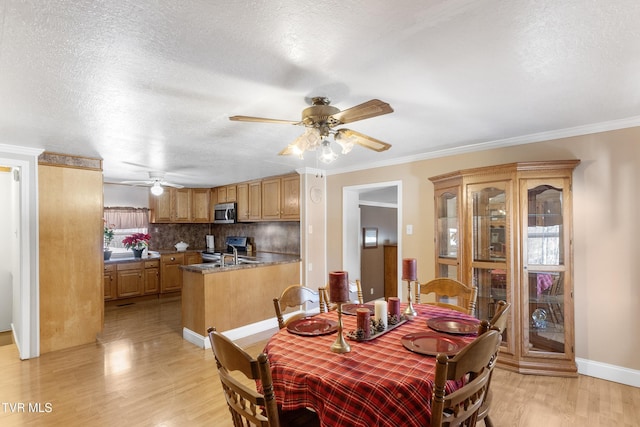 dining room featuring light wood finished floors, baseboards, ornamental molding, and a textured ceiling