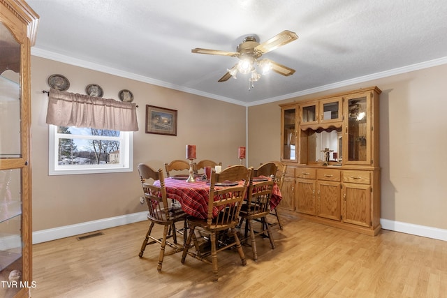 dining room with ceiling fan, visible vents, baseboards, light wood-type flooring, and crown molding