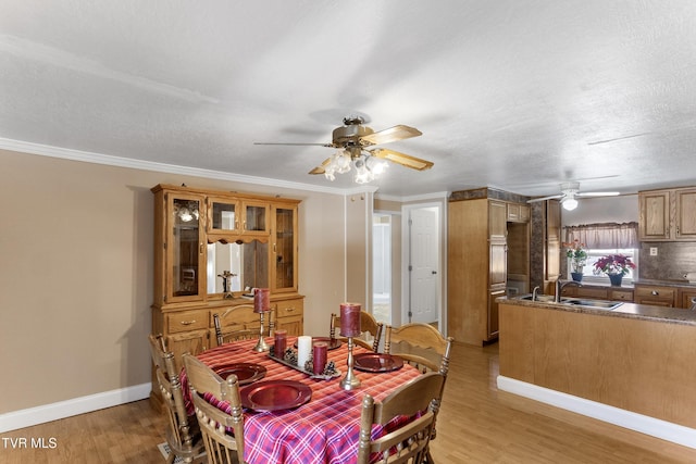 dining room featuring light wood-type flooring, crown molding, baseboards, and ceiling fan