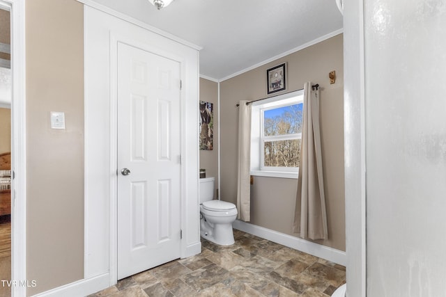 bathroom with stone finish floor, crown molding, baseboards, and toilet