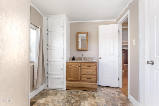 bathroom featuring stone finish floor, crown molding, vanity, and baseboards