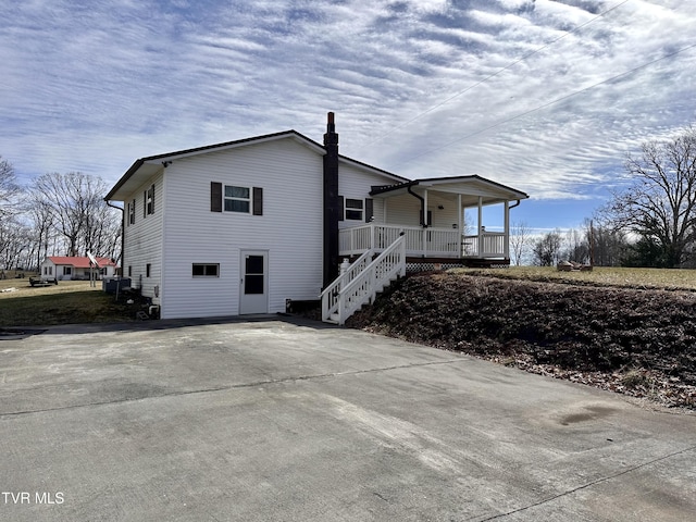 view of property exterior with covered porch, a chimney, stairs, and central air condition unit