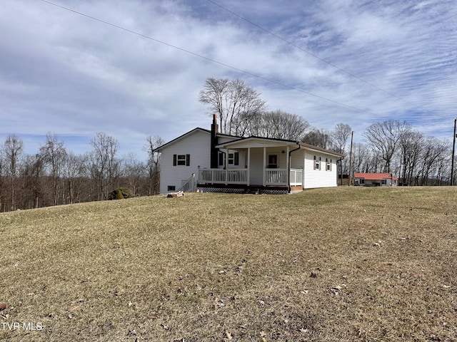 back of house with a chimney, a porch, and a lawn