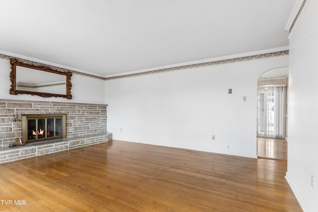 unfurnished living room featuring crown molding, a stone fireplace, and wood-type flooring