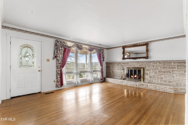 unfurnished living room with hardwood / wood-style flooring, ornamental molding, and a stone fireplace