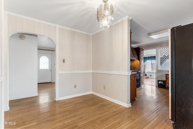 empty room with crown molding, an inviting chandelier, and light hardwood / wood-style floors