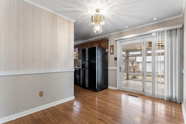 interior space with sink, a notable chandelier, crown molding, light wood-type flooring, and black refrigerator with ice dispenser