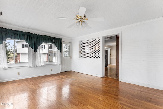 unfurnished room with hardwood / wood-style flooring, ornamental molding, brick wall, and ceiling fan