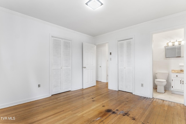 unfurnished bedroom featuring multiple closets, crown molding, ensuite bath, and light hardwood / wood-style floors