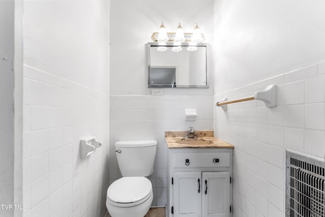 bathroom with heating unit, vanity, toilet, and tile walls