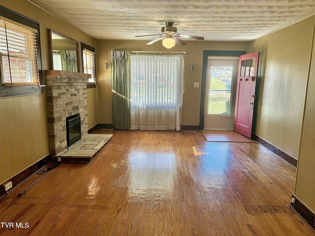 unfurnished living room featuring a stone fireplace, ceiling fan, light hardwood / wood-style flooring, and wooden walls