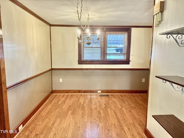 unfurnished dining area with a chandelier, ornamental molding, and light wood-type flooring