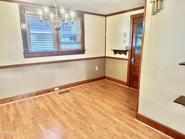 unfurnished dining area with a chandelier, light hardwood / wood-style floors, and ornamental molding