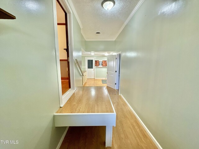 hallway with light hardwood / wood-style floors, a textured ceiling, and ornamental molding