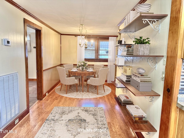 dining room with hardwood / wood-style flooring, crown molding, and an inviting chandelier