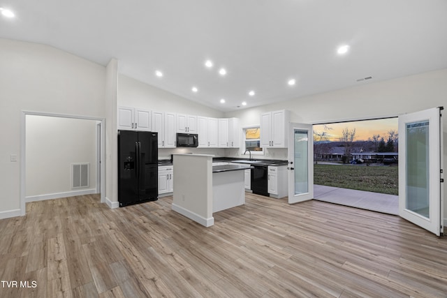 kitchen with black appliances, white cabinets, light wood-type flooring, and vaulted ceiling