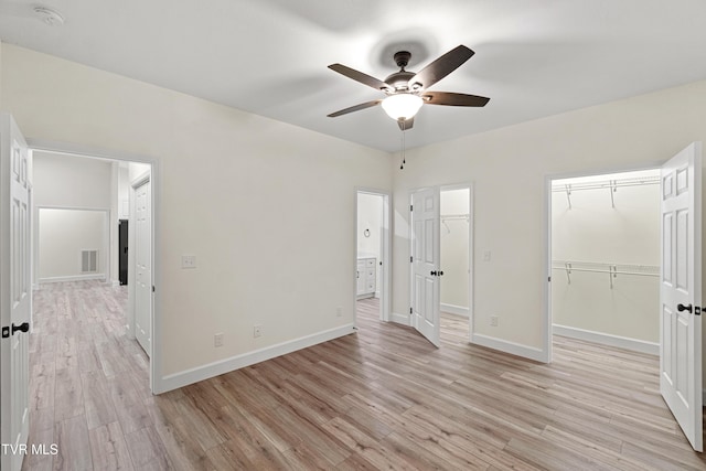 unfurnished bedroom with a walk in closet, ceiling fan, a closet, and light hardwood / wood-style floors