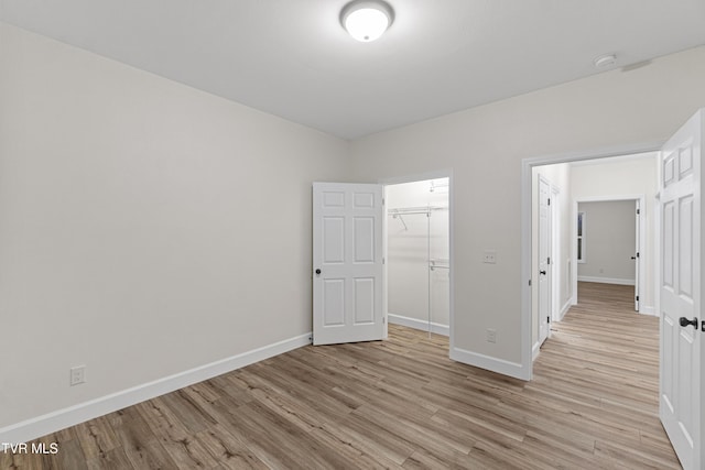 unfurnished bedroom featuring a walk in closet, a closet, and light wood-type flooring