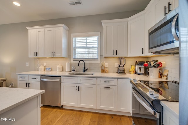 kitchen with sink, white cabinets, stainless steel appliances, and light hardwood / wood-style flooring