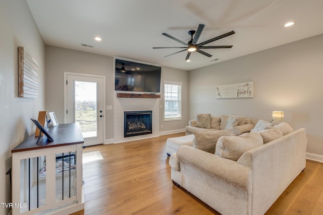 living room with a fireplace, light wood-type flooring, and ceiling fan