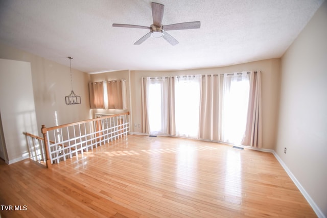 empty room with ceiling fan, plenty of natural light, a textured ceiling, and light wood-type flooring