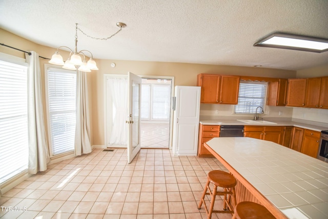 kitchen featuring a textured ceiling, pendant lighting, an inviting chandelier, dishwasher, and tile counters