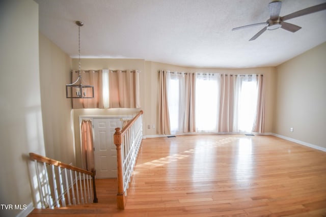 unfurnished living room featuring ceiling fan with notable chandelier and light hardwood / wood-style floors