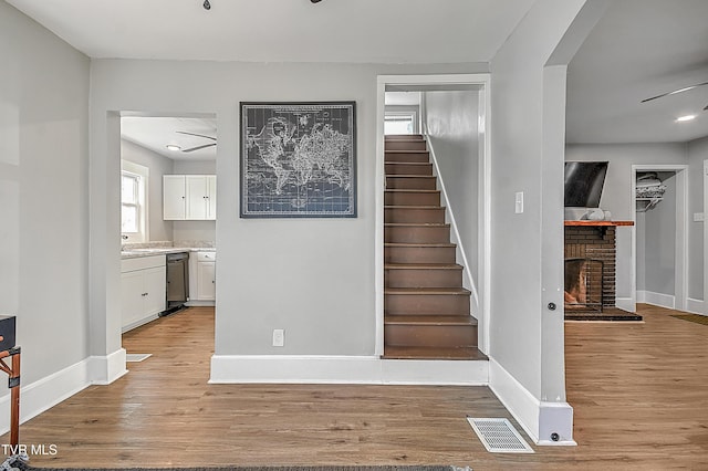 staircase with ceiling fan, a fireplace, hardwood / wood-style floors, and sink