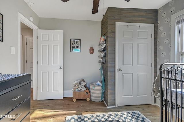 bedroom featuring hardwood / wood-style floors, ceiling fan, and a nursery area