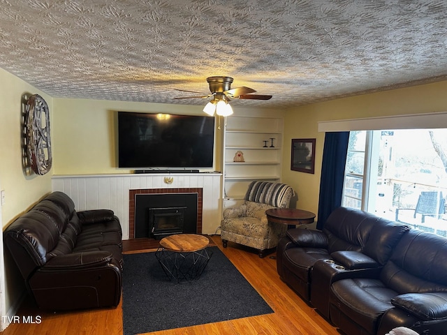 living room with hardwood / wood-style floors, a textured ceiling, a wood stove, and ceiling fan